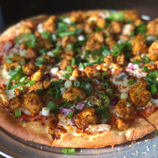 Fun Pizza Kitchen's chicken pizza with green onions, jalapeños, and red onions on a metal tray.