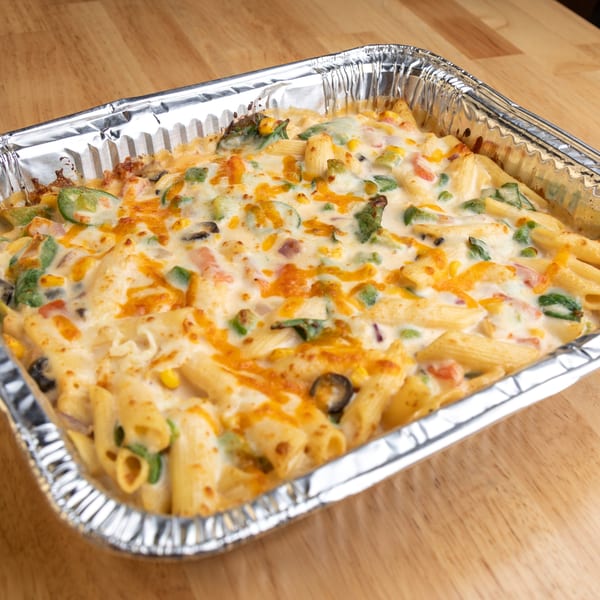 Baked penne pasta with melted cheese, green peppers, corn, and olives in a foil pan.