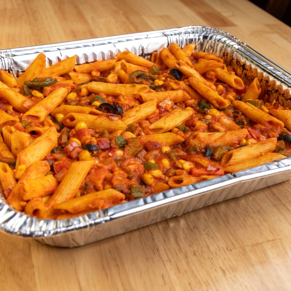 Penne pasta in a red sauce with corn, olives, and green peppers in a foil pan.