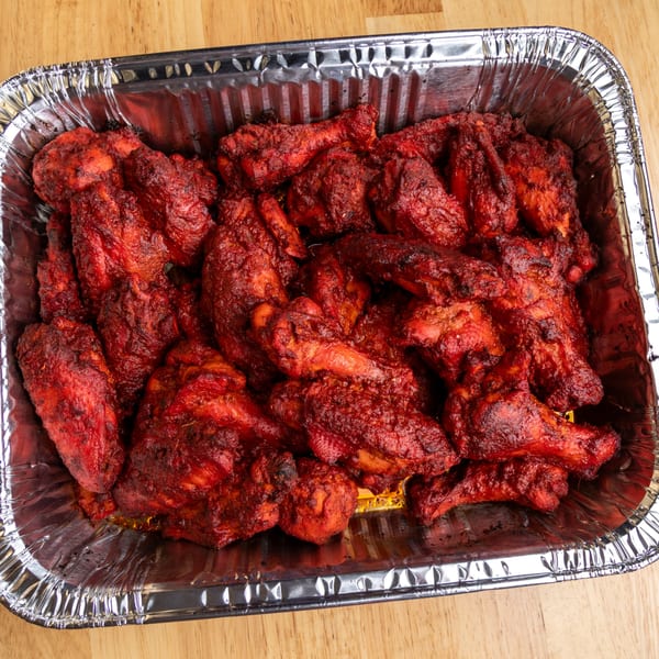 A foil pan filled with many bright red, saucy chicken wings from Fun Pizza Kitchen.