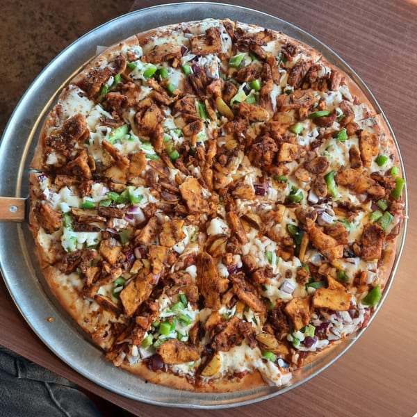 A Fun Pizza Kitchen pizza with chicken, green peppers, and onions on a metal tray.