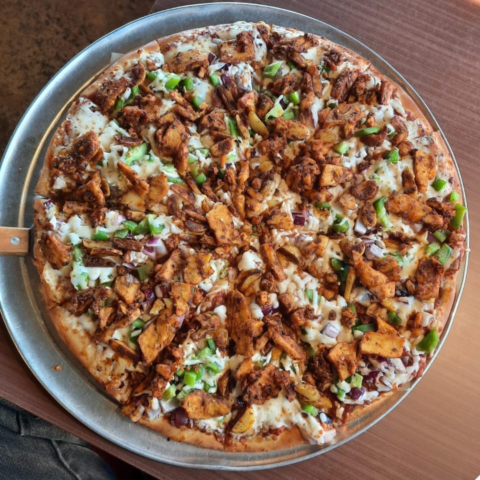 A Fun Pizza Kitchen pizza with chicken, green peppers, and onions on a metal tray.