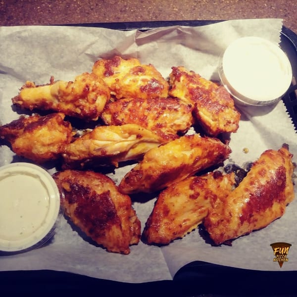 A basket of golden-brown chicken wings with two containers of dipping sauce on white parchment paper.